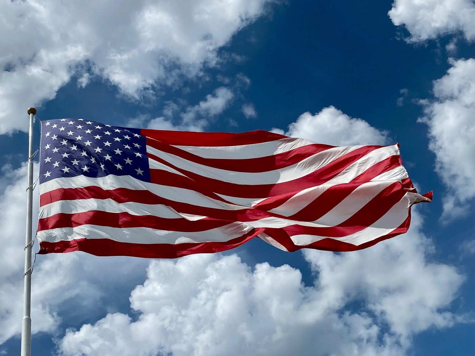 A close-up of the American flag waving against a vibrant blue sky with clouds.